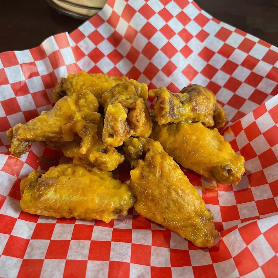 Golden chicken wings served in a red and white checkered paper-lined basket.