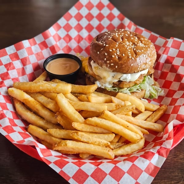 A burger with fries and dipping sauce in a red and white checkered basket.