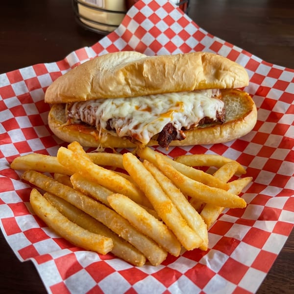 Meatball sub with melted cheese and a side of golden fries on red and white checkered paper.